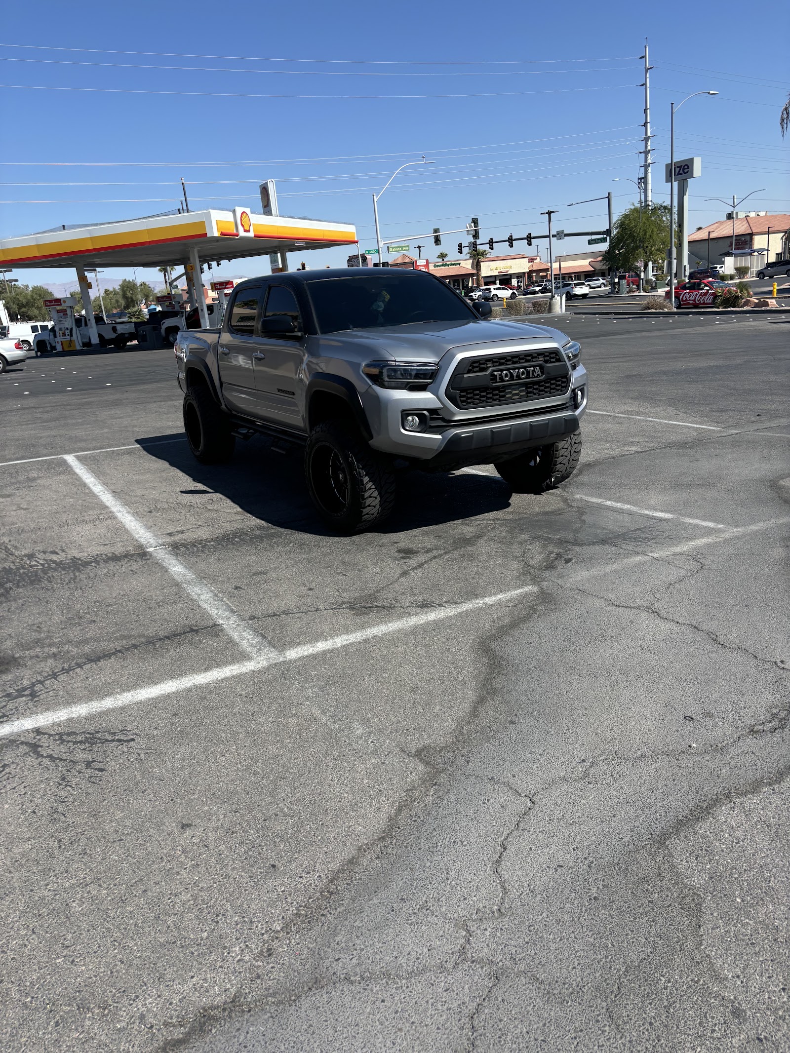 Lifted silver Toyota Tacoma TRD with dark tinted windows at a gas station